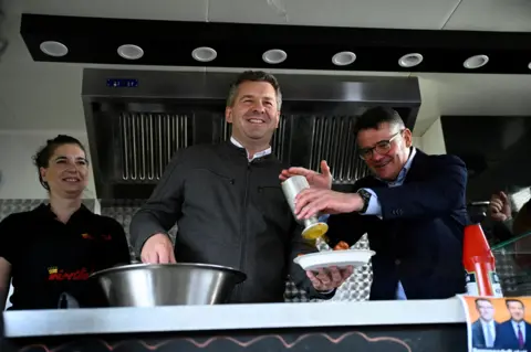 Reuters Sven Schulze (centre), together with Hesse State Premier Boris Rhein (right), serves currywurst with fries, during a campaign event in Magdeburg, Germany,