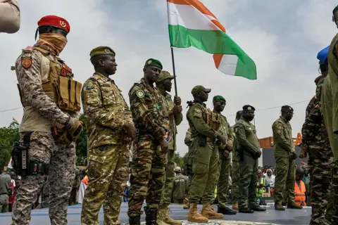 AFP via Getty Images A line of soldiers in camouflage stand on a stage - one of them, in the centre, is holding up a Niger flag.