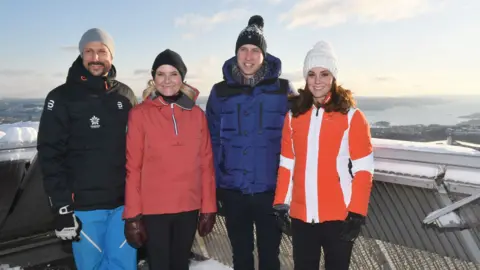 Getty Images Four people stand smiling at the camera in ski jackets and woollen hats. On the left is a man with a goattee beard and next to him is a woman with blonde hair. Next is Prince William wearing a blue ski jacket and pom-pom hat, and Kate wearing a bright orange jacket and white hat. They are standing outside and look to be high-up on a mountain, and in the background is snow and a view.