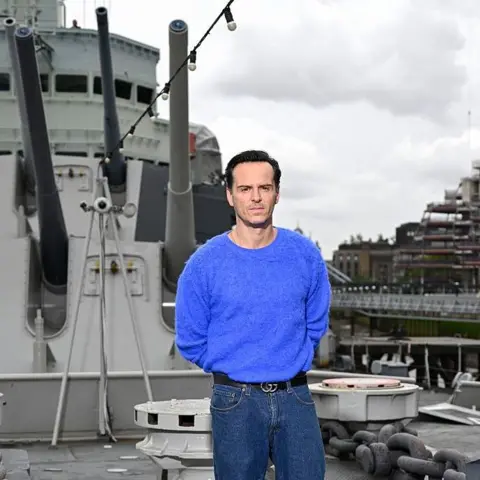 Getty Images Andrew Scott in a blue jumper and jeans on HMS Belfast