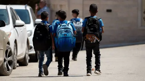 Palestinian kids walk to school. They are wearing blue school uniforms. 