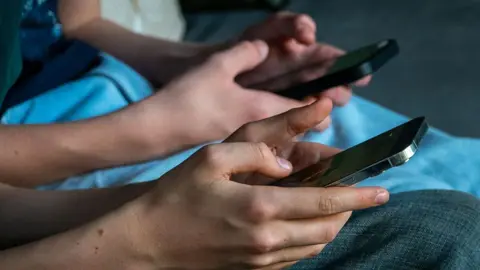 Getty Images A close-up image of two people sitting together, using their smartphones