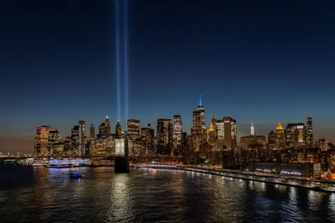 Getty Images Manhattan skyline at night with the skyscrapers all lit up against a dark sky. Two beams of light are emitted from One World Trade Center to commemorate the twin towers that were destroyed in 2001