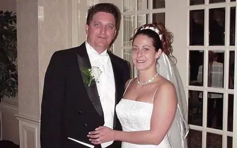 Tom Resta John on the left is in his wedding suit with a flower in his lapel. Sylvia is on the right in a wedding dress and tiara. They are both smiling at the camera.