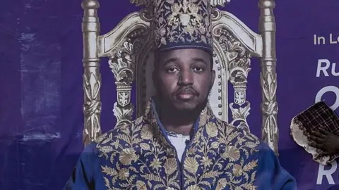 AFP via Getty Images A portrait of King Oyo wearing an elaborate blue-and-gold ceremonial robe and matching crown sits on an ornate throne 