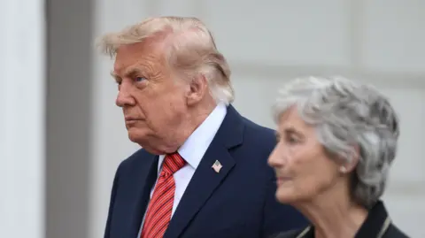 Reuters Donald Trump, light grey hair, in dark suit, red tie, is standing beside Irish President Catherine Connolly who has short grey hair and is wearing a black suit.