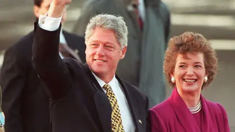 Getty Images A man with grey hair and black suit waves, beside him a woman with brown hair smiles, she is wearing a pink suit