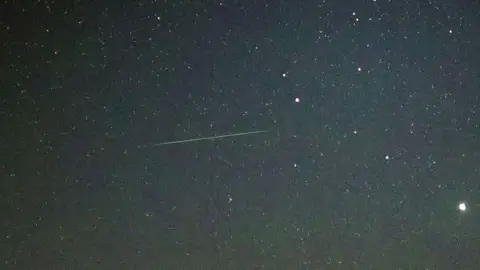 Getty Images A green line cuts through a starry sky, capturing a meteor passing through the atmosphere. 