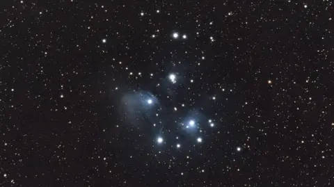 Getty Images A group of stars shine bright white in the middle of starry black night sky. 