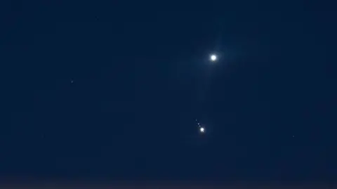 Getty Images In a dark blue, almost black, sky the two planets of Jupiter and Venus shine brightly in the distance.