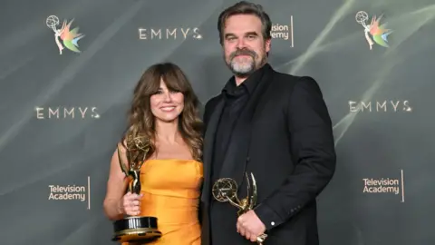 Getty Images US actress Linda Cardellini, wearing an orange dress, and US actor David Harbour, in a black suit, pose with their Emmys for outstanding supporting actress and actor in a limited or anthology series or movie for DTF St. Louis.  