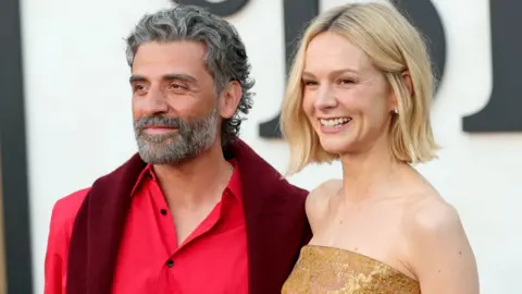 Getty Images Oscar Isaac, wearing a red shirt, and Carey Mulligan, waring a gold sequinned dress, attend the Los Angeles premiere of Netflix's Beef season two in Los Angeles