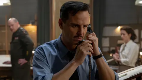 Alex Bailey/Focus Features/StudioCanal Andrew Scott in a wartime shirt with a small moustache and clipped, short hair - he is on the phone on the set of the film, looking tense