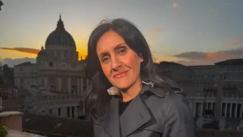 Maryam Moshiri  Maryam Moshiri stand in a black coat. The Vatican is in the background