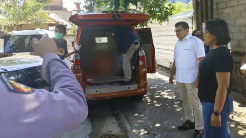 Supplied: Indonesia police A person stands inside the rear end of an orange van while several other people stand beside the vehicle