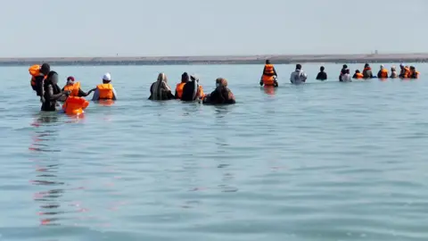 A group of migrants wade through seawater on the beach in Gravelines, in a grab from the BBC video.