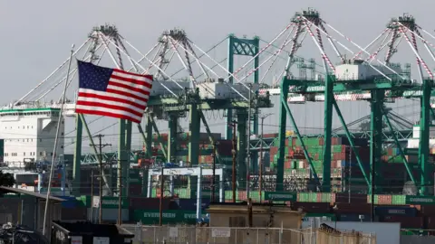 EPA/Shutterstock An American flag waves against a backdrop of cranes and storage containers in Los Angeles.