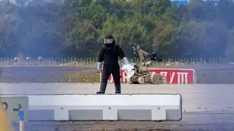 Getty Images A police investigator works on the tarmac with a robot capable of defusing explosives near a Ukrainian Antonov cargo plane at Leipzig/Halle Airport on 5 August