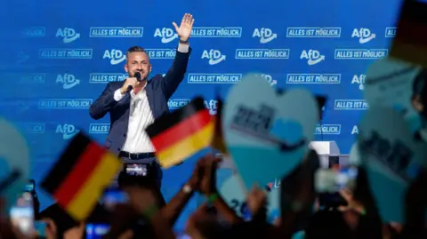 Getty Images Ulrich Siegmund, lead candidate of the far-right Alternative for Germany (AfD), gestures as he speaks to supporters during an AfD-sponsored outing of Simson motorcycle enthusiasts ahead of upcoming state elections in Saxony-Anhalt on July 26, 2026 in Weissenfels, Germany. 