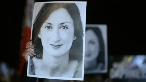 MATTHEW MIRABELLI/AFP via Getty Images Protesters hold a black and white picture of the late journalist Daphne Caruana Galizia