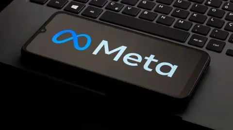 Getty Images A photo of a phone kept on a laptop keyboard. The phone is displaying the logo of the company Meta