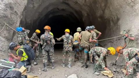 Nepal Army/Reuters People in camouflage clothing and wearing helmets stand at the entry to a tunnel