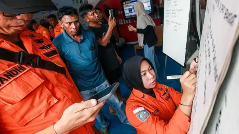 Getty Images Relatives of affected passengers look on as a National Search and Rescue Agency (Basarnas) officer writes updates on a whiteboard amid ongoing rescue operations on the stricken Virgo Transport 8 ferry, at Trisakti Bandarmasih Port in Banjarmasin, South Kalimantan, on September 13, 2026.