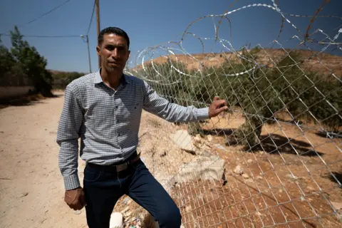 Waheed Abu stands by school barbed wire. 