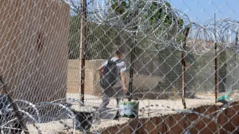 EPA/Shutterstock A Palestinian boy, seen through a security fence bordering the school campus, leaves on the first day of the new academic year, in the village of al-Mughayyir, near Ramallah, West Bank. Photo: 6 September 2026