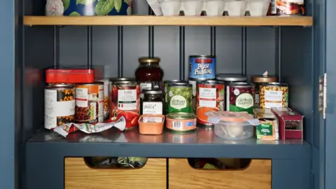 Getty Images A cupboard filled with jars and tins of food.