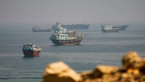 Reuters Several ships sit in a large body of water, with fog on the horizon and blurred rocks in the foreground.