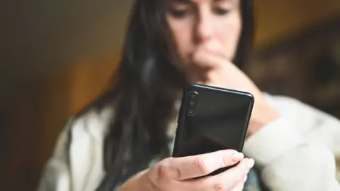 Getty Images A stock image of a woman looking down at her smartphone, biting her nails nervously