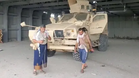 AL MASIRAH/Handout via REUTERS Screengrab of a video from Houthi-run Al Masirah TV showing an armed man walks next to an armoured vehicle in Mocha, Yemen, after the Houthis reportedly seized the Red Sea port city (10 September 2026)